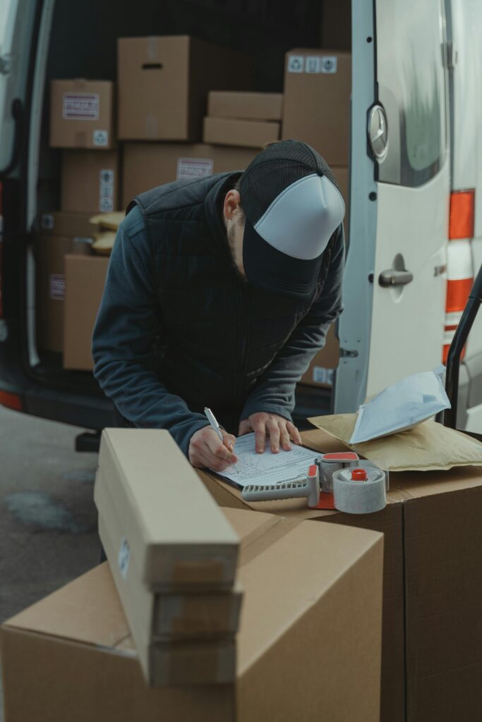 pexels-photo-6169057-6169057 Courier organizing packages from a van, preparing for delivery in a logistics setting.